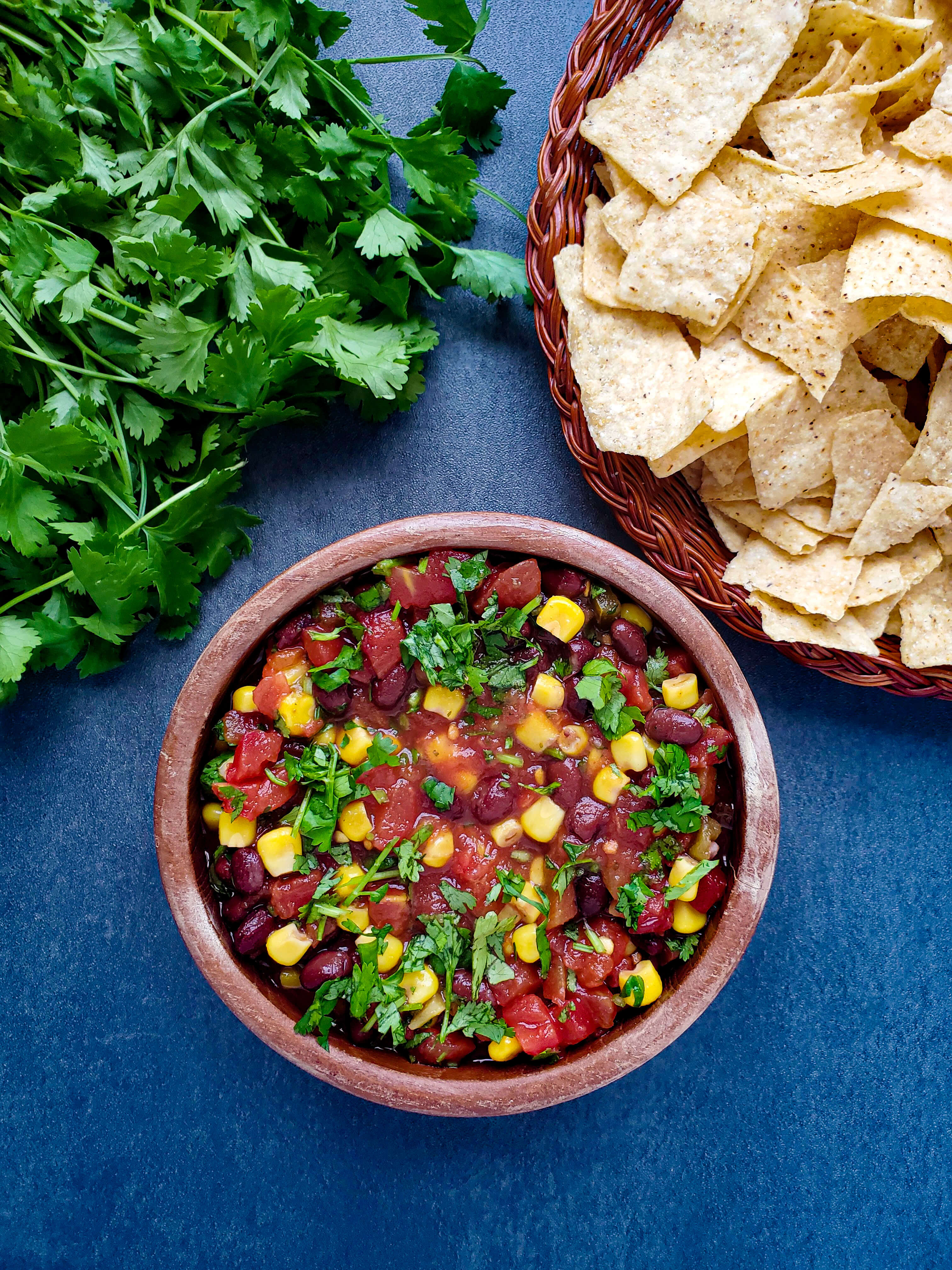 bowl of black bean and corn salsa with fresh cilantro and tortilla chips above the bowl