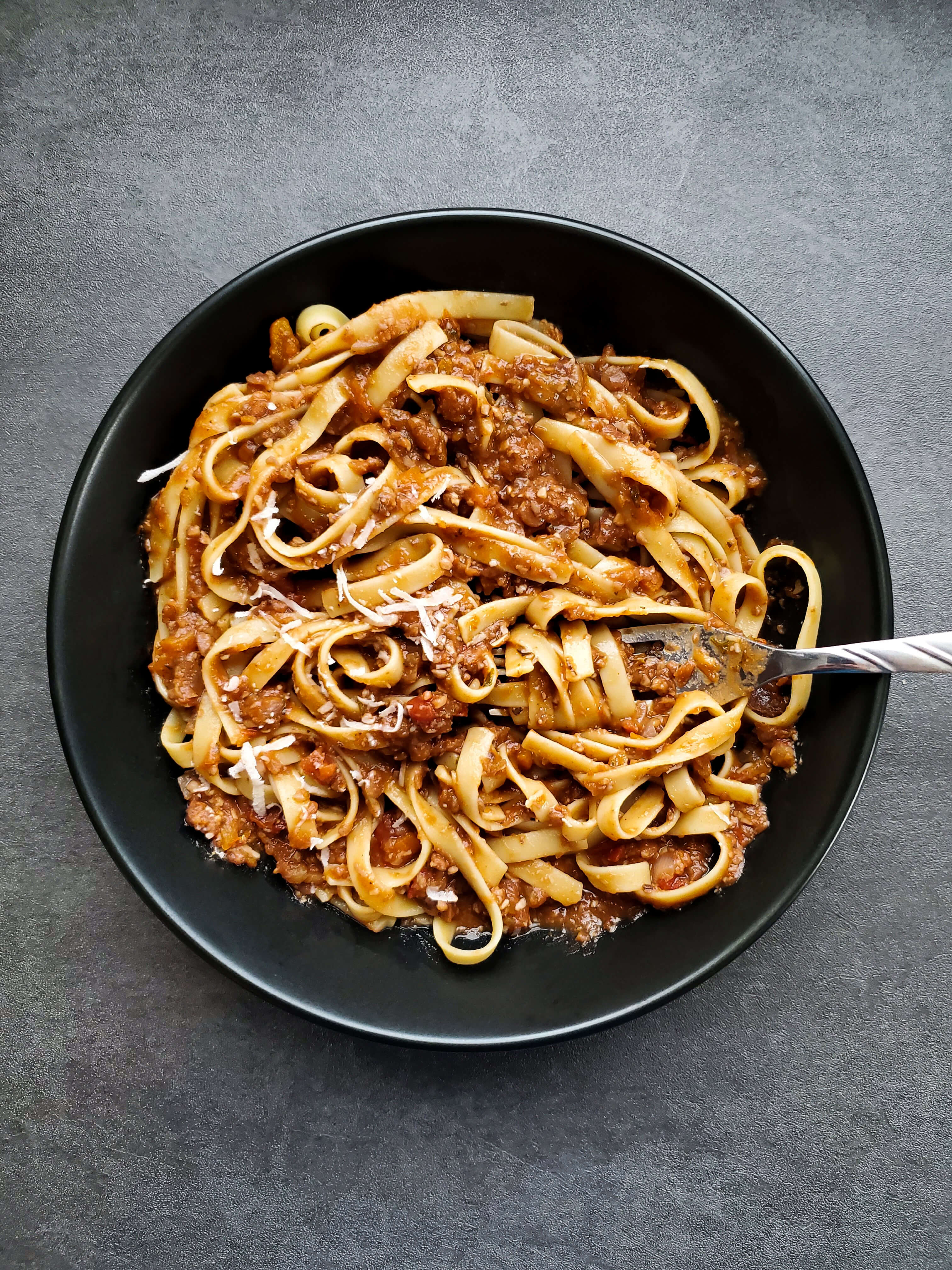 a black bowl with spaghetti noodles and lentil bolognese sauce