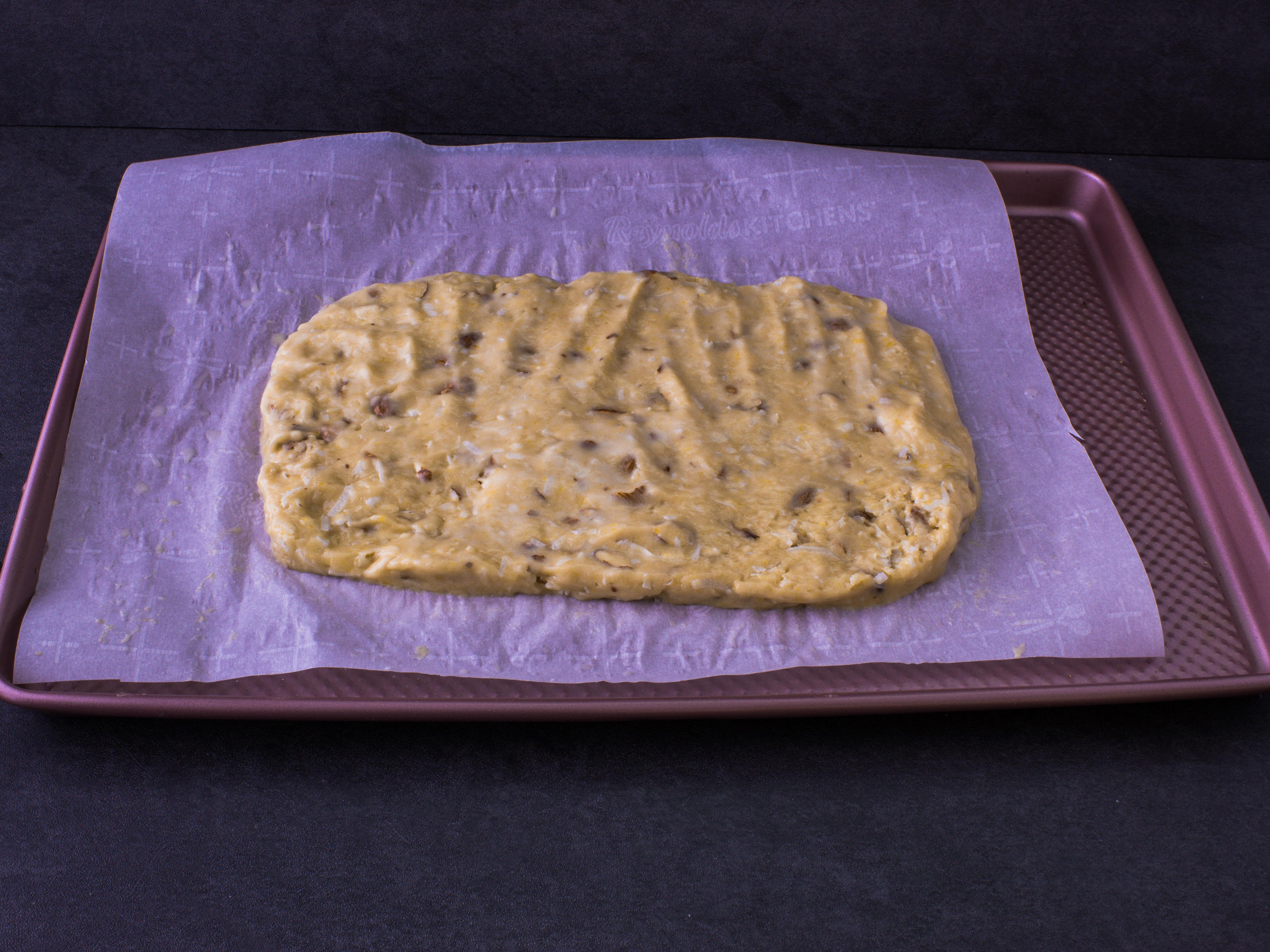 a baking sheet lined with parchment paper, with flattened coconut biscotti dough shaped into a rectangle