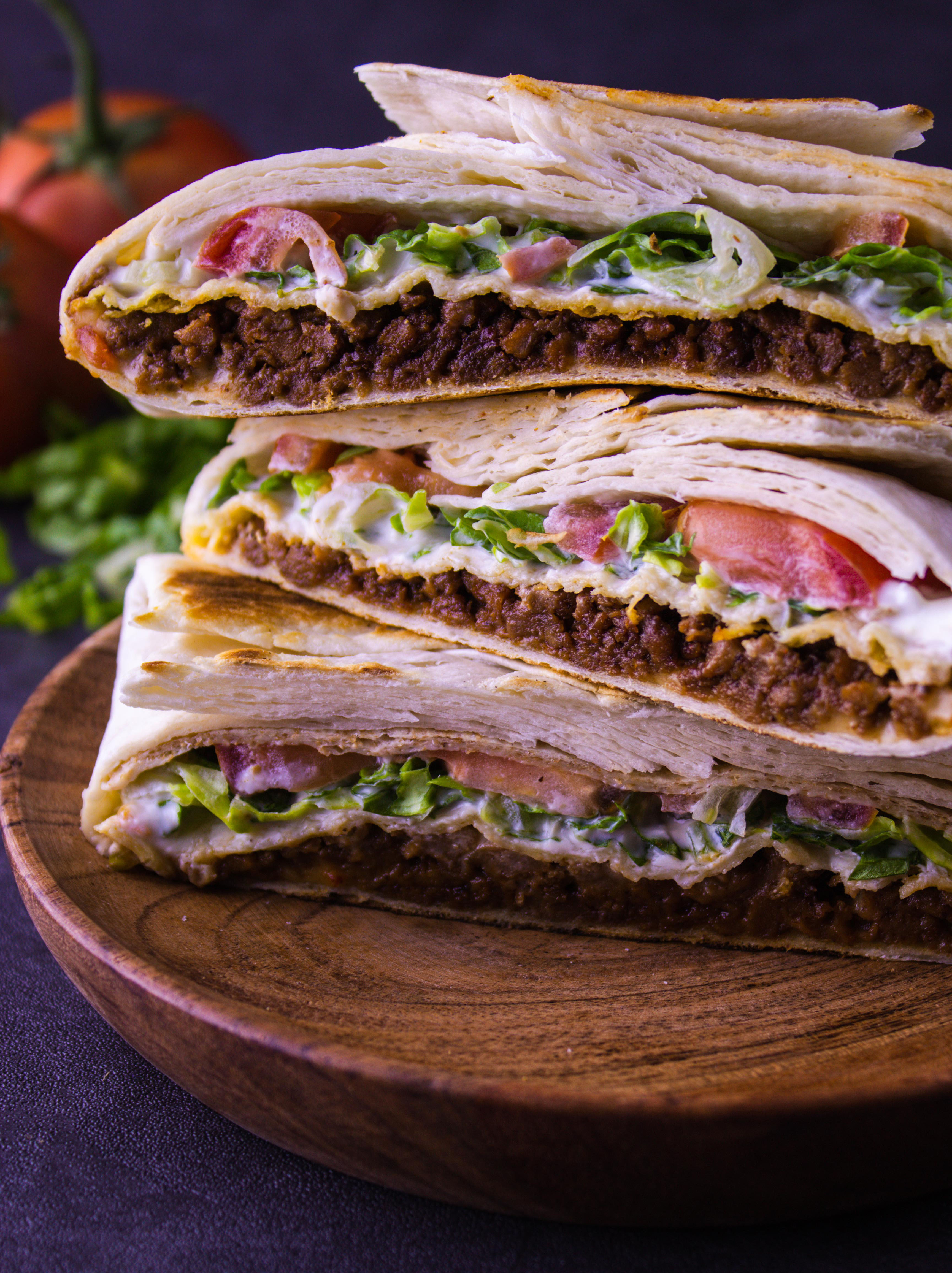 wooden plate stacked high with 3 crunchwraps and tomatoes and lettuce in the background